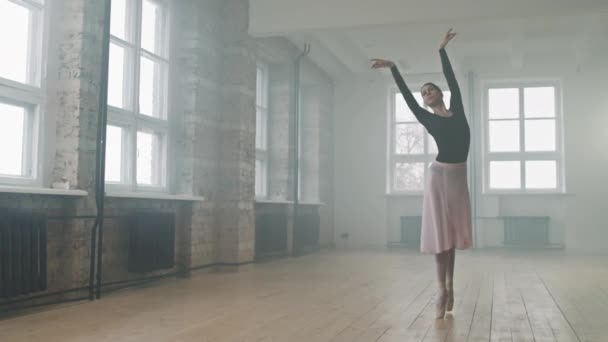 Pełen strzał utalentowanej młodej baleriny tańczącej z wdziękiem w pustym studio tańca wypełnionym dymem, cieszącej się procesem - Materiał filmowy, wideo