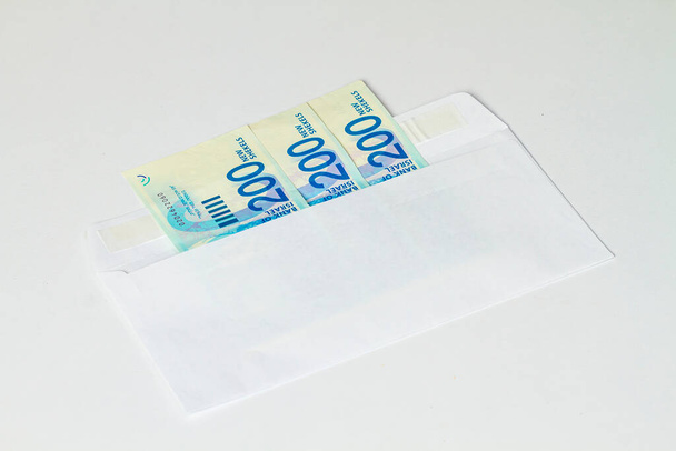 Tres billetes de 200 nuevos shekels israelíes están en un sobre de correo sobre un fondo claro. - Foto, imagen