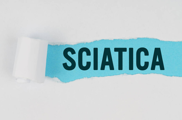 Medicine and health concept. In the middle of a white sheet of paper, a tear is made under which, on a blue background, the inscription - SCIATICA - Φωτογραφία, εικόνα