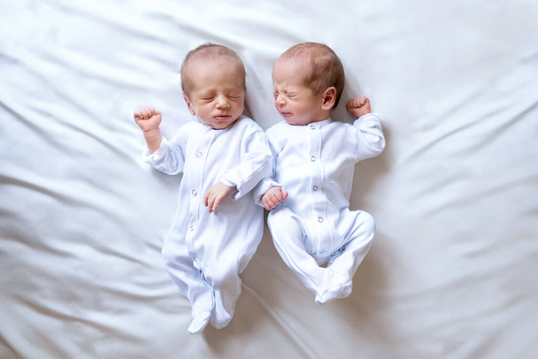 Pasgeboren tweelingen op het bed, in de armen van hun ouders, op een witte achtergrond. Levensstijl, emoties van kinderen. Meerlingzwangerschap. De grote familie - Foto, afbeelding