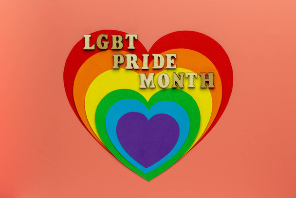 Ουράνιο τόξο heards συμβολίζουν γκέι και ΛΟΑΤ υπερηφάνεια σε ένα ροζ φόντο. LGBT PRIDE μήνα. Μια φράση από ξύλινα γράμματα. - Φωτογραφία, εικόνα