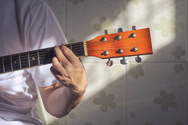 Сонячне світло і тінь на поверхні руки хлопчика-підлітка, що практикує грати на гітарі вдома
 - Фото, зображення
