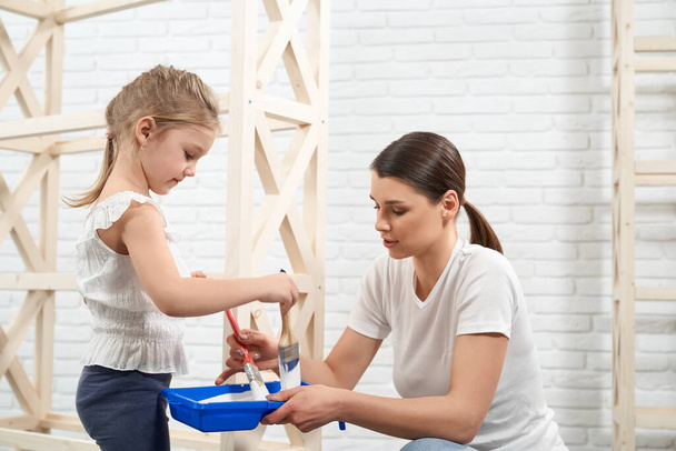 Young brunette with child preparing dye for painting rack. - Φωτογραφία, εικόνα