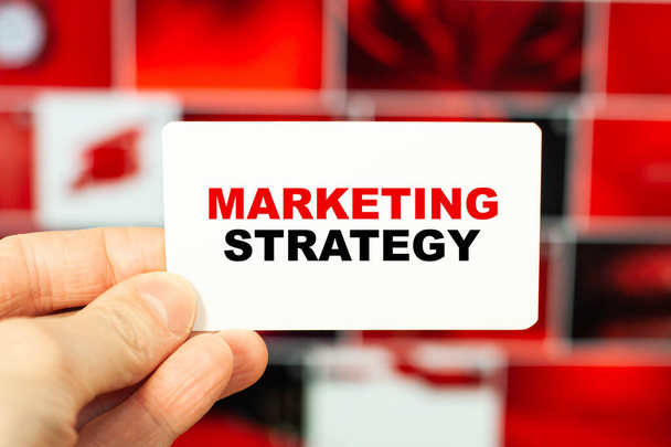 Ένας άνθρωπος κρατά μια επαγγελματική κάρτα σε κόκκινο φόντο με τις λέξεις - Στρατηγική μάρκετινγκ - Φωτογραφία, εικόνα