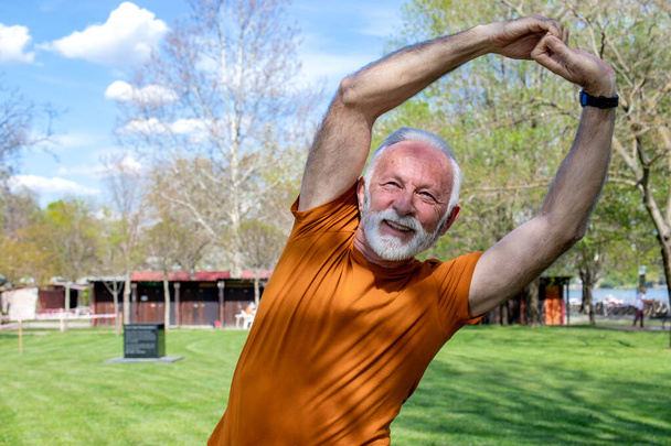 Happy energetic senior retired man stretching in the park, doing side bends exercise. Close up. - Photo, Image