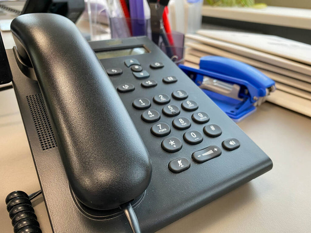 Чорний пластиковий офісний стаціонарний телефон з кишеньковим пристроєм та кнопками для вирішення бізнес-задач та здійснення дзвінків на переговори
. - Фото, зображення