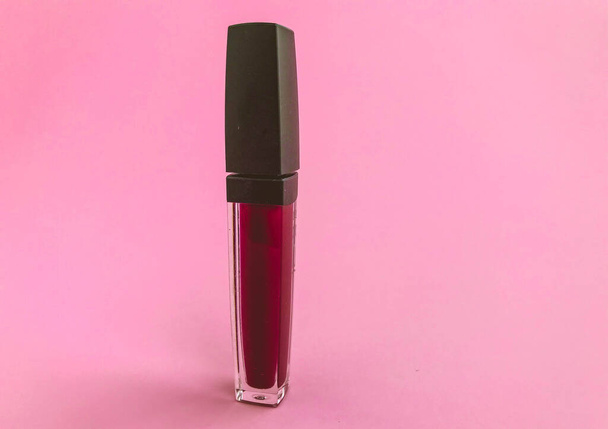 Hermosa belleza cosmética glamoroso líquido rojo mate lápiz labial en un tubo con una esponja para aplicar textura para aplicar maquillaje en los labios sobre un fondo rosa delicado. - Foto, Imagen