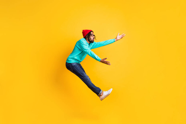 Full size profile photo of brunette optimistic guy jump catch wear cap spectacles pullover jeans isolated on yellow background - Fotografie, Obrázek