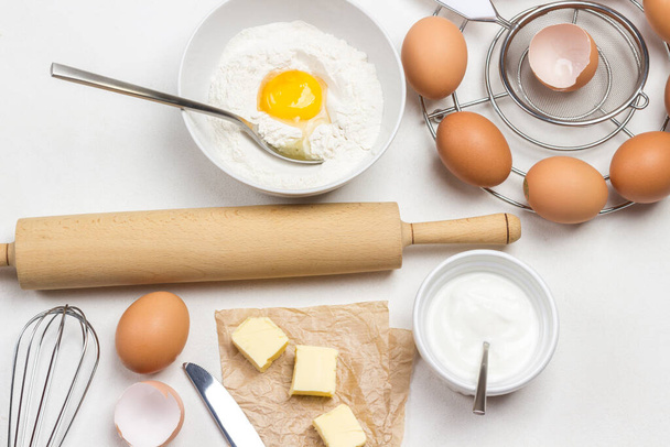 Rolling pin for dough. Broken egg and flour in bowl. Butter and chicken eggs. White background. Flat lay - 写真・画像