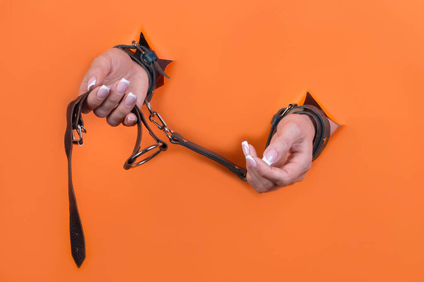 Adult sex toys, minimal design, isolated on an orange background. Women's hands in handcuffs. Bdsm. - Fotó, kép