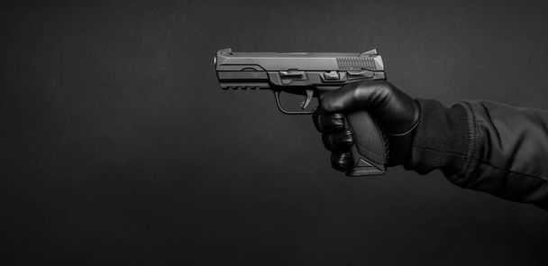 A man's hand in a black leather glove holds a pistol. Weapon in the hand of a man on a dark background. Weapon threat. - Fotó, kép