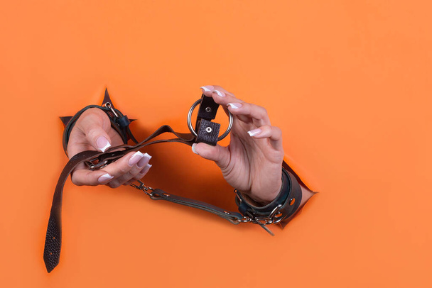 Adult sex toys, minimal design, isolated on an orange background. Women's hands in handcuffs. Bdsm. - Photo, Image