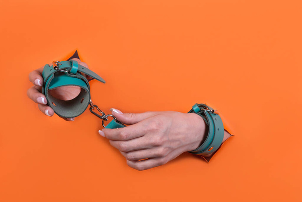 Adult sex toys, minimal design, isolated on an orange background. Women's hands in handcuffs. - Foto, afbeelding