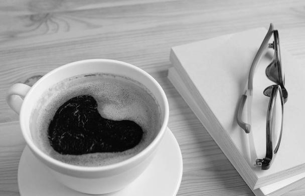 Schiuma a forma di cuore primo piano di caffè nero con libri e bicchieri in monocromo - Foto, immagini