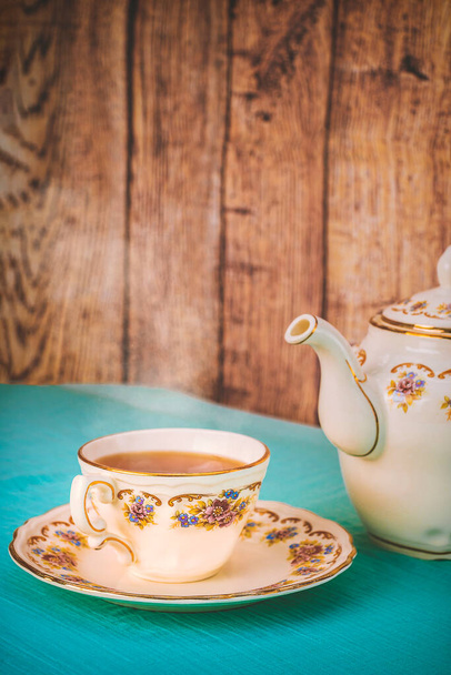 Vista de una taza de té y una tetera de porcelana fina sobre una mesa al atardecer - Foto, imagen