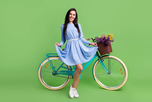 Photo of confident funny young woman dressed blue outfit holding dress skirt bike smiling isolated green color background - Photo, image