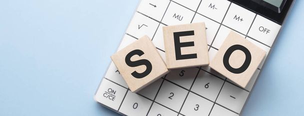 SEO - word made up of wooden cubes on a white background between a black pen and a calculator. Business concept - Foto, afbeelding