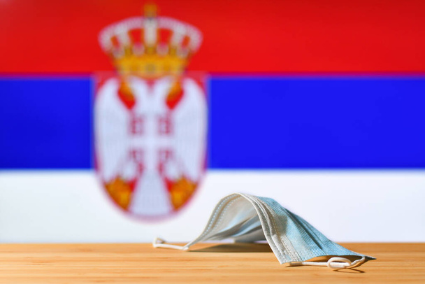 Tegen de achtergrond van de vlag van Servië ligt een medisch masker op tafel. Het concept van een verplichte maskerregeling voor inwoners van het land en toeristen in Servië tijdens een pandemie. - Foto, afbeelding