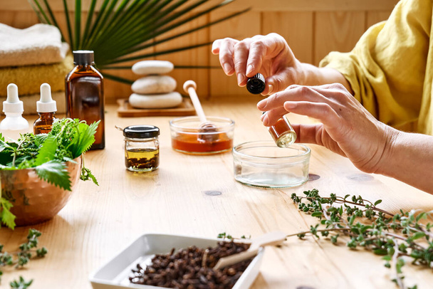 Woman prepares aromatherapy session at the table with essential oil diffuser medical herbs, different types of oils and essences. Aromatherapy and alternative medicine concept. Natural remedies. - Fotoğraf, Görsel