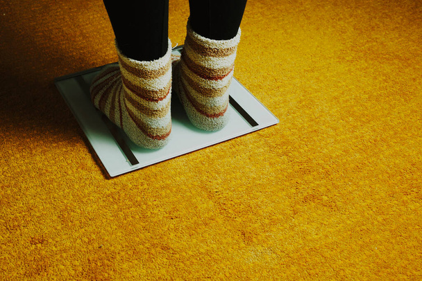 женские ноги с носками и весами на желтом ковре - Фото, изображение