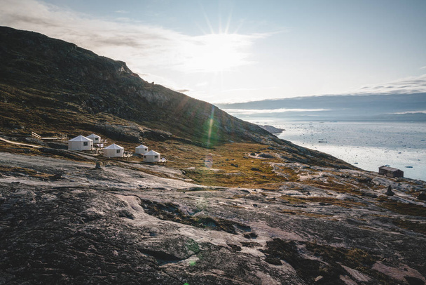 Panoramic image of Camp Eqi at Eqip Sermia Glacier in Greenland. nature landscape with lodge cabins. Midnight sun and pink sky. Tourist destination Eqi glacier in West Greenland AKA Ilulissat and - Foto, afbeelding