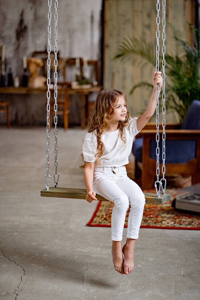pretty girl in white clothes rides on swing. original childrens room - Foto, imagen