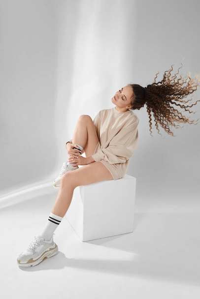 Beautiful model girl with long sexy legs and perfect slim body wearing a trendy sweatshirt and modish sneakers posing over white background in studio - Fotoğraf, Görsel