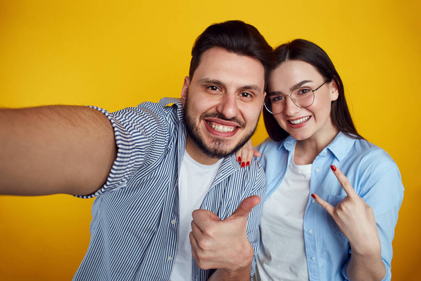 Couple takes selfie on cellular, makes like gestures over yellow background - Fotoğraf, Görsel
