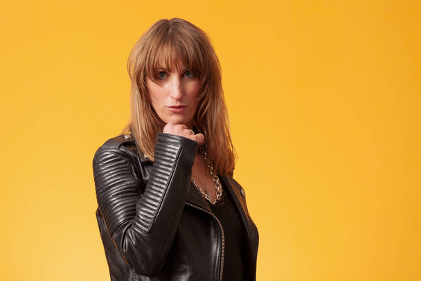 Portrait of a beautiful woman wearing a black leather jacket in front of a yellow backdrop - Fotó, kép