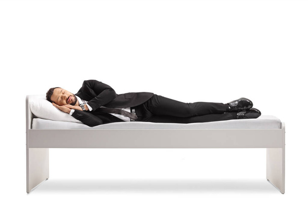 Full length shot of a businessman in a suit and tie sleeping on a bed isolated on white background - Foto, afbeelding