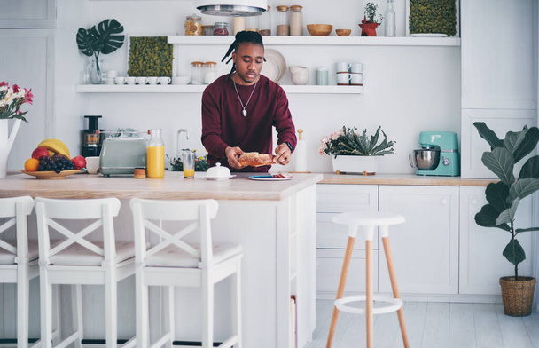 young african american man busy with morning routine on kitchen at home, preparing breakfast before leave - Fotó, kép
