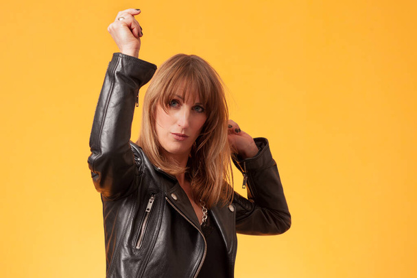 Portrait of a beautiful woman wearing a black leather jacket in front of a yellow backdrop - Foto, Imagem