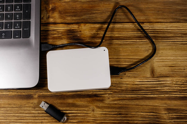 Внешний жесткий диск, подключенный к ноутбуку и USB флешке на деревянном столе. Вид сверху. Концепция хранения данных - Фото, изображение