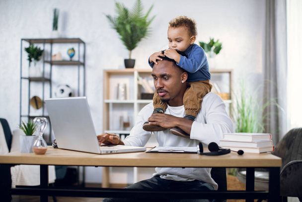 Afro american man with son on neck working on laptop - Foto, Imagem