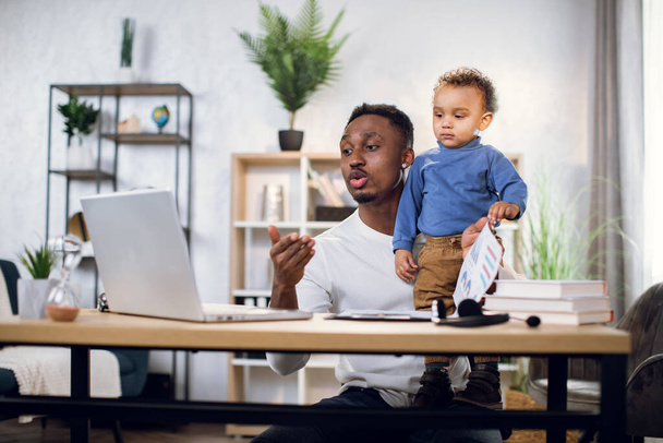 African businessman working from home with son on hands - Foto, imagen