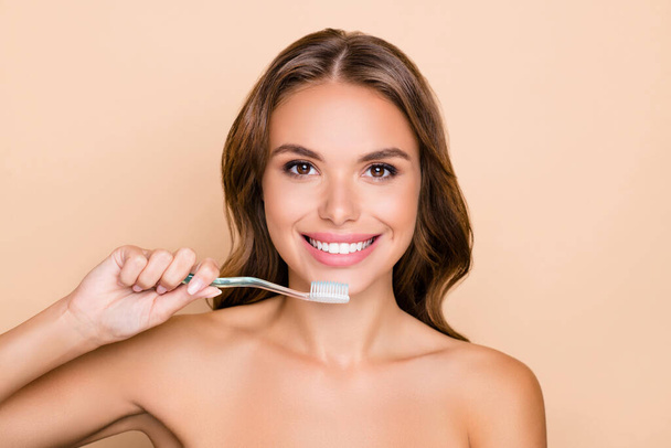Photo of young happy positive smiling girl with naked shoulders brushing teeth morning routine isolated on beige color background - Photo, image