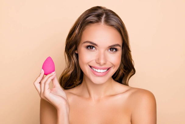Photo of young attractive lovely smiling girl with no clothes holding beauty blender isolated on beige color background - 写真・画像