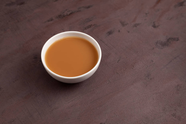 Traditional Tibetan butter tea or churned tea in white bowl. Selective focus. Asian drink known as "Po Cha" blend of black tea yak butter and salt. Brown background, copy space. - Photo, image