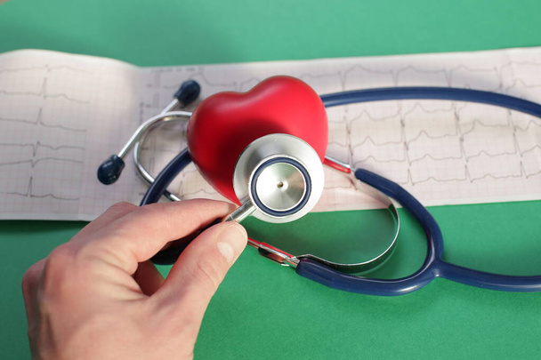 Artsen hand met medische stethoscoop hart en cardiogram op groene achtergrond - Foto, afbeelding