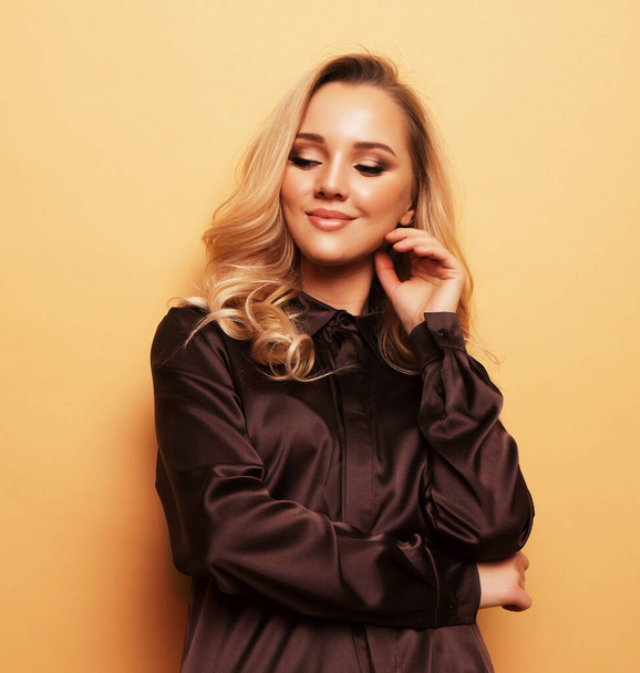 Stylish blond woman in blouse and pants posing on beige background. - 写真・画像