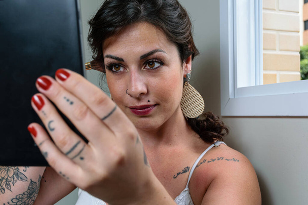 Closeup of tattooed Brazilian woman putting on makeup and using a tablet. - Φωτογραφία, εικόνα