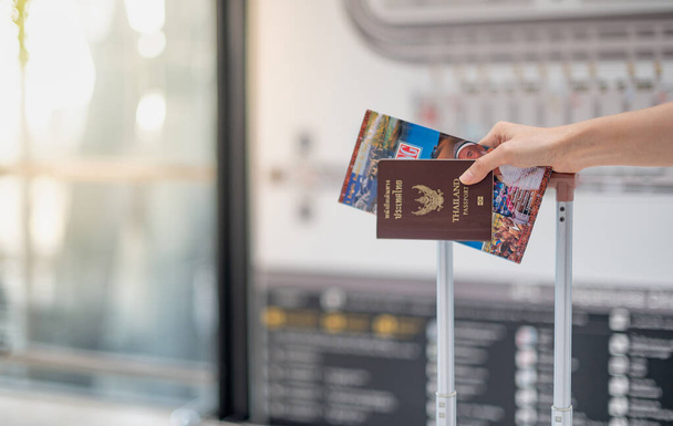 Female hand holding passport book and travel guide book  while hand carrying luggage suitcase at the airport, Due to the Covid-19 Epidemic pandemic concept. - Photo, Image