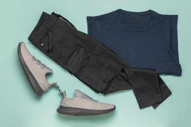 Een paar grijze sneakers, een zwarte broek en een trui op een blauwe achtergrond. Fashionable jeugd casual kleding. - Foto, afbeelding