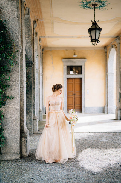 Mariée dans une belle robe avec un bouquet de fleurs roses se dresse dans un couloir voûté près de la verdure. Lac de Côme, Italie - Photo, image