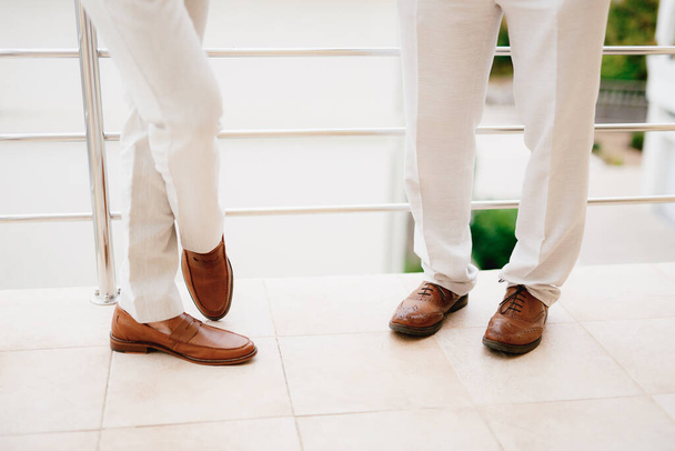 As pernas de dois homens em pé na varanda, close-up. O noivo e seu padrinho durante a preparação para a cerimônia de casamento.  - Foto, Imagem