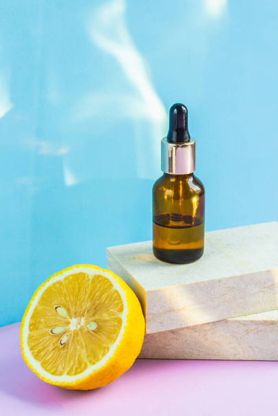 A cosmetic jar with an eyedropper stands on two granite slabs, like on catwalks, next to half a yellow lemon and the glare of the sun on the background. Cosmetics for summer. - Photo, Image