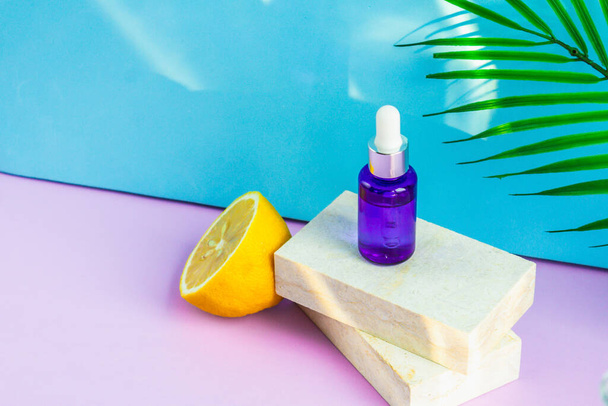 A cosmetic jar with an eyedropper stands on two granite slabs, like on a catwalk, next to half a yellow lemon, a palm leaf and the glare of the sun in the background. Cosmetics for summer. - Fotoğraf, Görsel