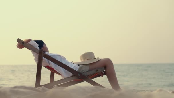 Mladá Asiatka se dívá na výhled na moře, jak se natahuje s pocitem zvednutých paží a odpočívá na lehátku na pláži. Rekreační letní koncept. - Záběry, video