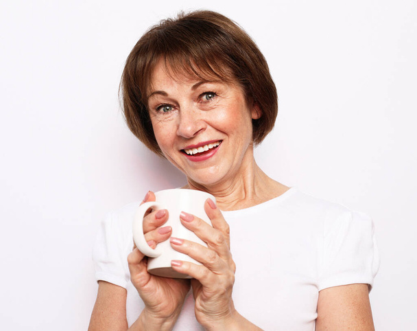 Cheerful elderly woman wear casual with cute smile holding a cup of coffee over white background. - Fotografie, Obrázek