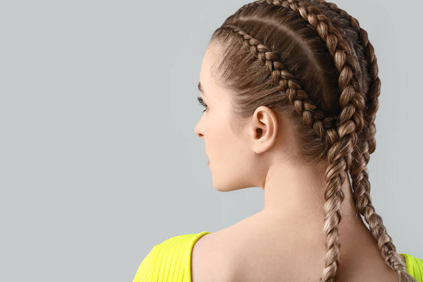 Beautiful young woman with braided hair on grey background - Photo, Image